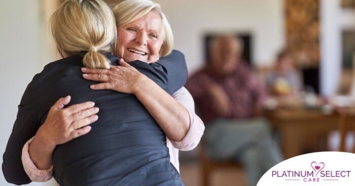 An older woman smiles as a younger woman visits her and hugs her, showing the effect that acts of kindness can have on senior loved ones.