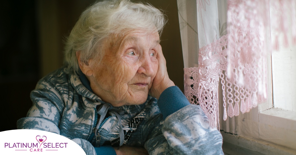 An older woman peacefully looks out of the window while the sun is still up, representing what can happen with sundowning.