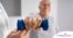 An older man is helped to lift a weight as part of physical therapy.